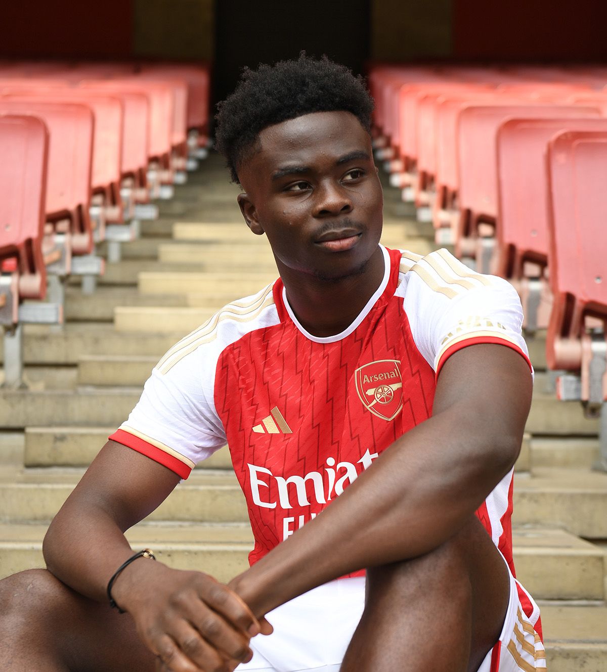 An image of Bukayo Saka in our 2023/24 home shirt sitting in a gangway inside Emirates Stadium